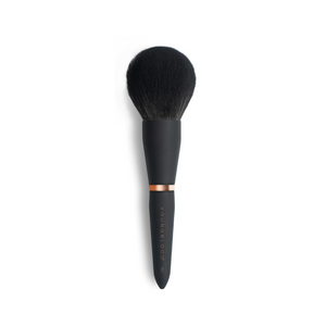 A large, tapered makeup brush with a black handle and synthetic bristles, designed for applying loose and pressed powders.